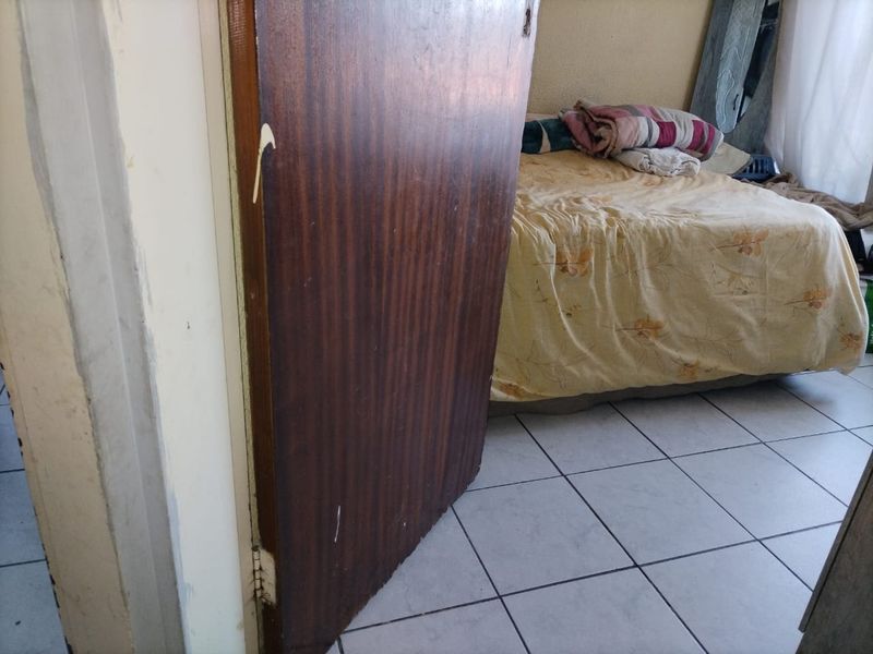A bedroom featuring tiled flooring and a wooden door, currently showing signs of wear and tear on the door and frame.