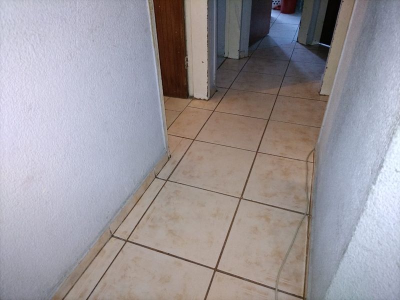 A narrow residential hallway featuring tiled flooring and multiple internal door access points, showing signs of wear and dated finishes.