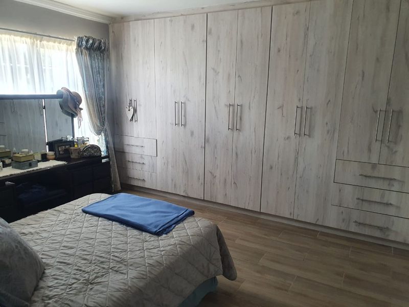 A well-maintained bedroom featuring extensive built-in cupboards with a light wood finish and modern tiled flooring.