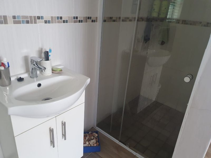 A functional bathroom featuring a white vanity cabinet with a basin, chrome mixer tap, and a glass-enclosed shower with decorative mosaic wall tiling.
