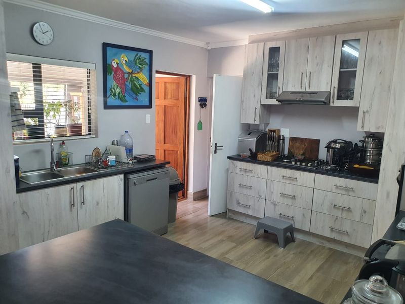 A functional kitchen featuring light wood-look cabinetry, dark countertops, a gas hob with extractor fan, and a double basin sink.