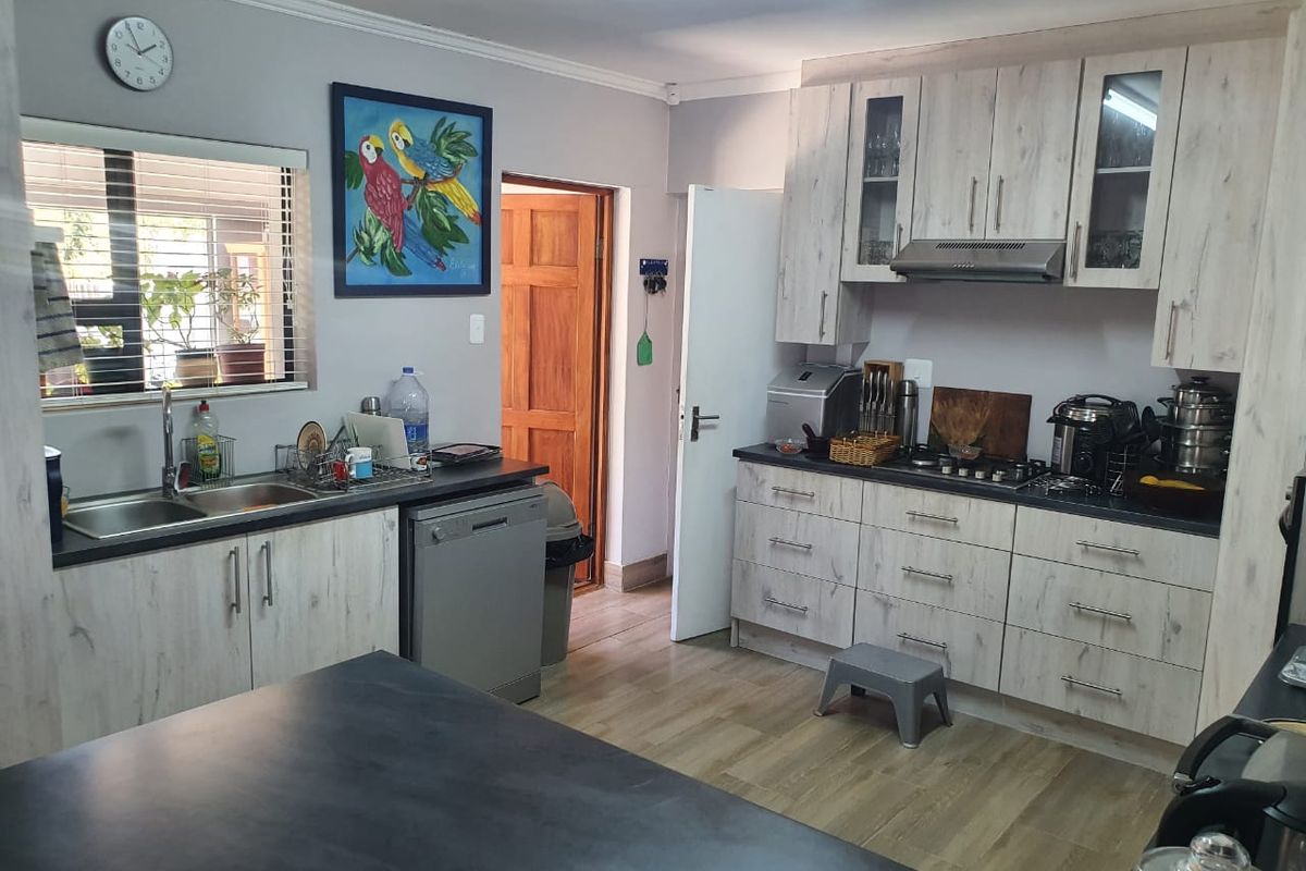 A functional kitchen featuring light wood-look cabinetry, dark countertops, a gas hob with extractor fan, and a double basin sink.