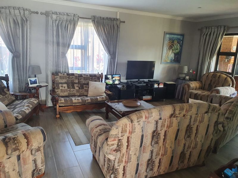 A comfortable living room featuring tiled flooring, recessed downlighting, and large windows with curtain rails, providing a functional and well-lit space.