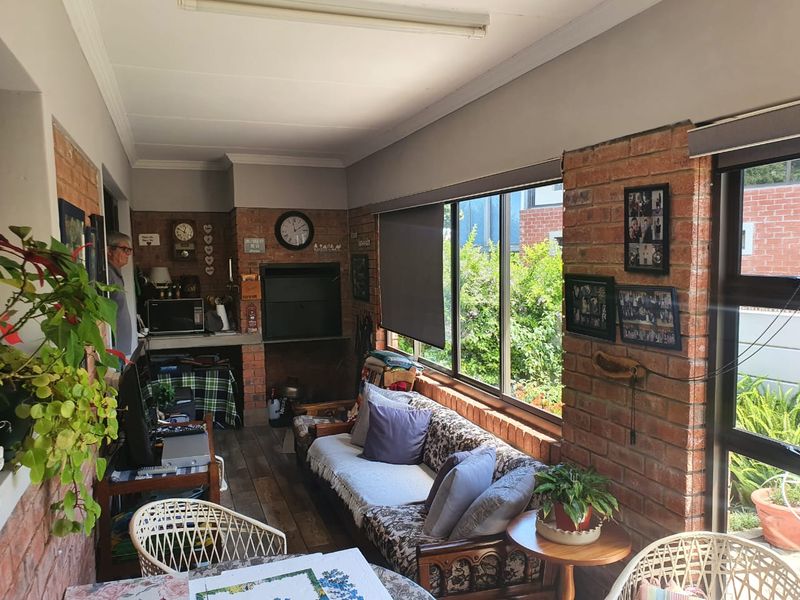 Enclosed patio area featuring exposed brick walls, large windows overlooking the garden, and a built-in braai, offering a versatile space for relaxation.