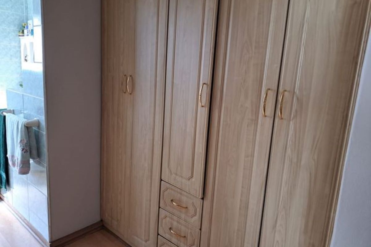 A bedroom featuring built-in wooden cabinetry with integrated drawers and gold-tone hardware, adjacent to a tiled bathroom area.
