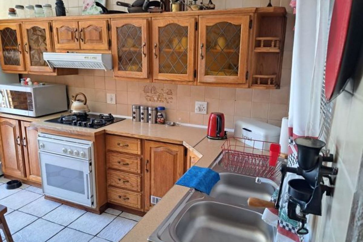 A functional kitchen featuring traditional timber cabinetry, a built-in gas hob, oven, extractor fan, and a double stainless steel sink with tiled splashbacks.