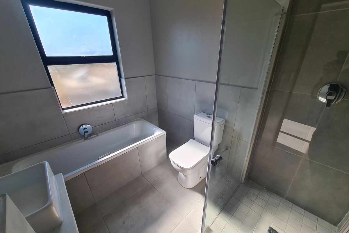 Modern bathroom featuring a built-in bathtub, separate glass-enclosed shower, toilet, and vanity basin with neutral grey tiling throughout.
