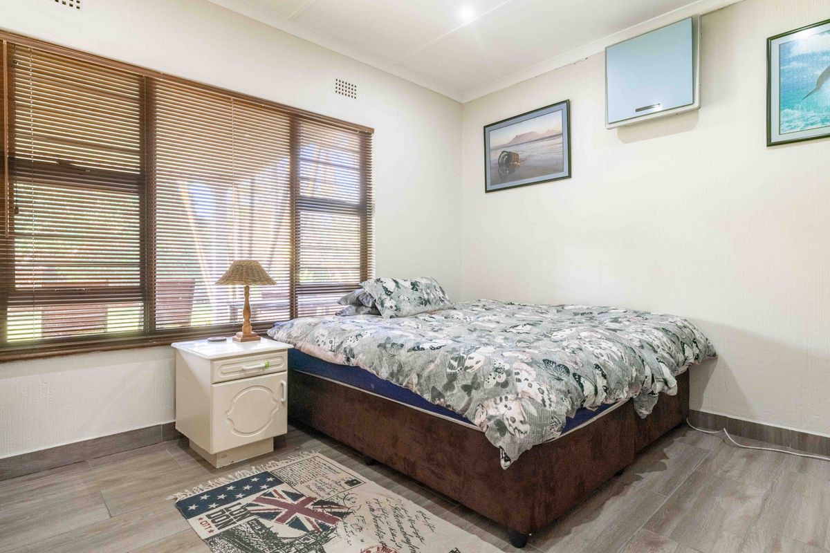 A bedroom featuring wood-look tile flooring, large windows with fitted blinds, and a wall-mounted air conditioning unit.