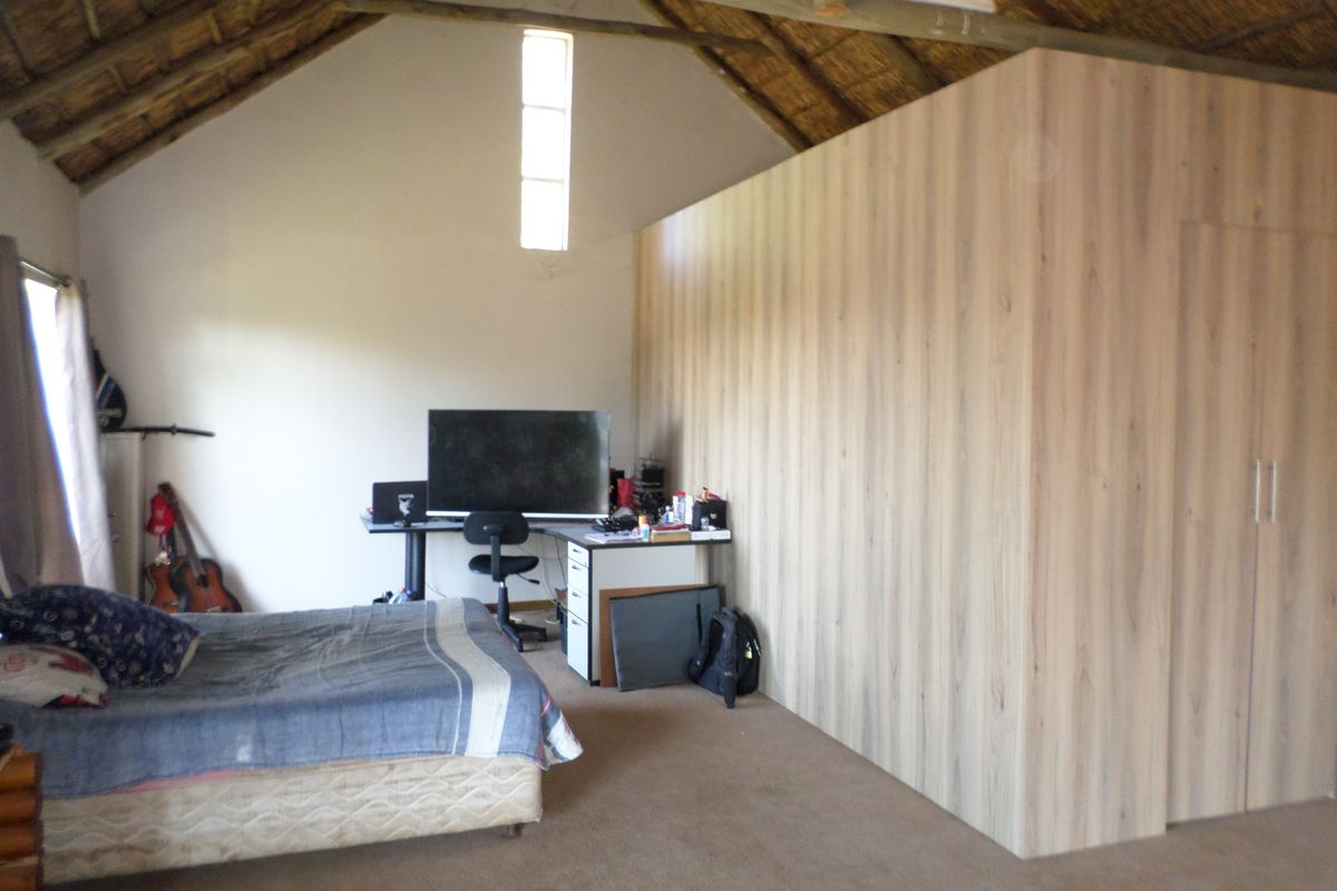 Spacious bedroom featuring a high-pitched thatch roof with exposed timber rafters and modern built-in cabinetry.
