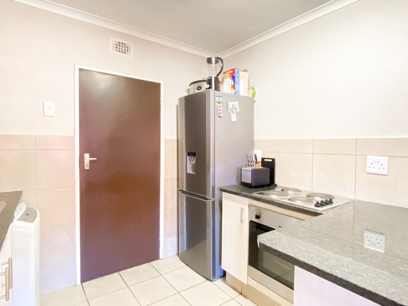 A functional kitchen featuring fitted cabinetry, a built-in oven with electric hob, double sink, and neutral tiled splashbacks.