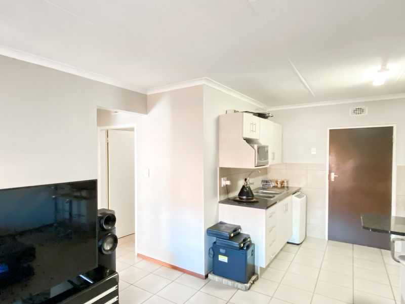 Open-plan living and kitchen area featuring tiled flooring, neutral walls, and functional built-in cabinetry with laminate countertops.