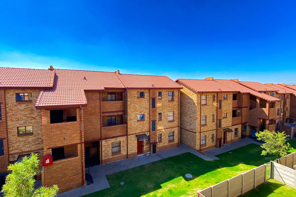 Exterior view of a multi-story apartment complex featuring face brick construction, tiled roofing, and well-maintained communal garden areas with paved walkways.