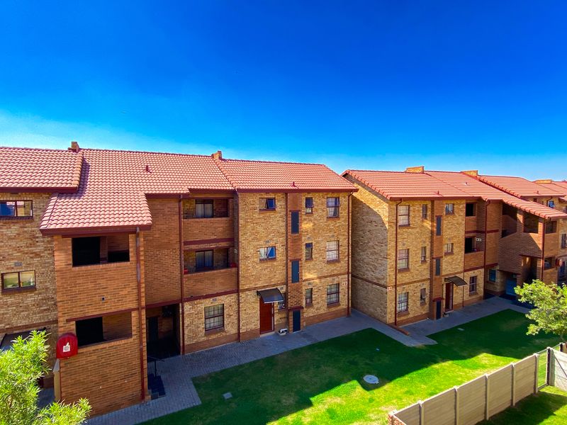 Exterior view of a multi-story apartment complex featuring face brick construction, tiled roofing, and well-maintained communal garden areas with paved walkways.