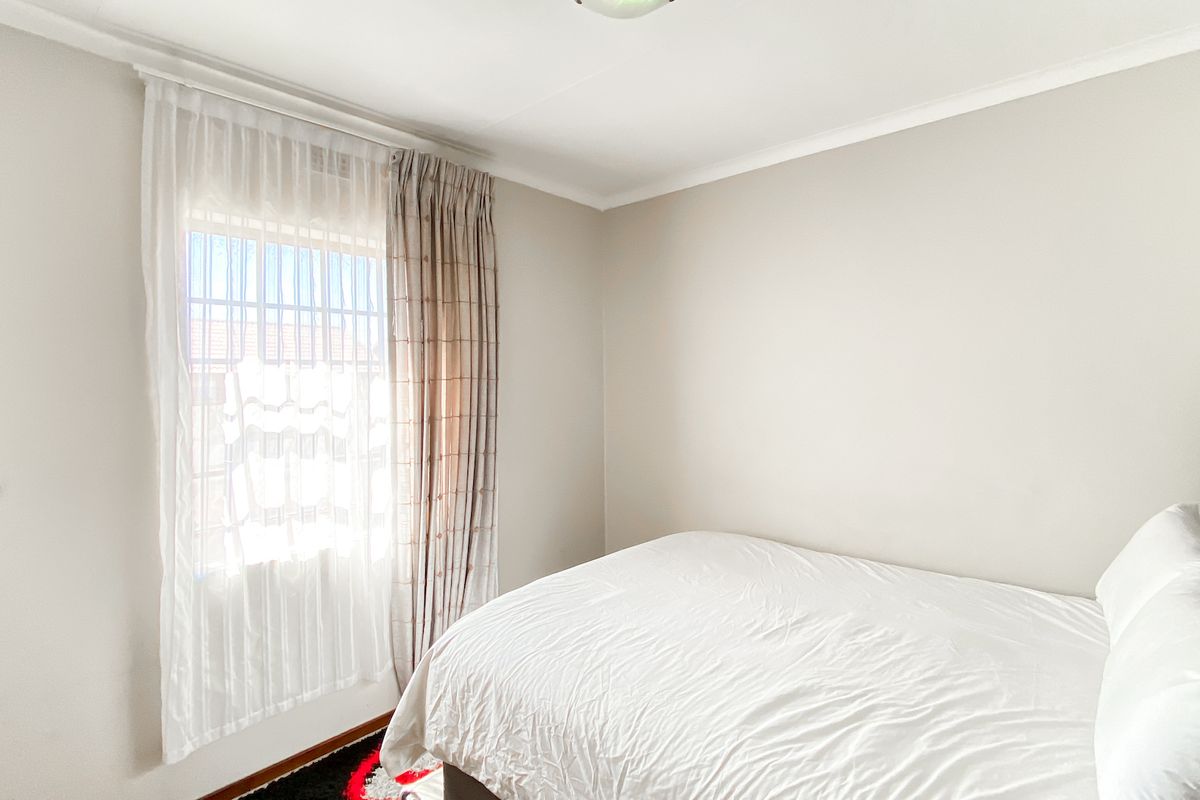 A bright and neutral bedroom featuring a window with security bars and installed curtain tracks, providing a clean and functional living space.