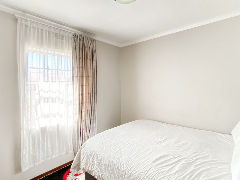 A bright and neutral bedroom featuring a window with security bars and installed curtain tracks, providing a clean and functional living space.