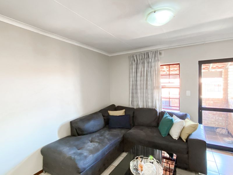 A living room featuring tiled flooring, neutral walls, and direct access to an outdoor area through an aluminium framed glass door.