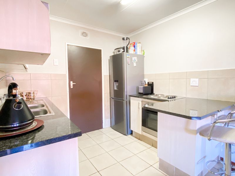 Functional kitchen featuring granite countertops, built-in oven, hob, and tiled finishes. The space offers a practical layout with integrated storage and preparation areas.
