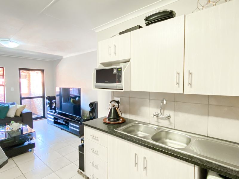 Open-plan living area featuring a functional kitchen with built-in cabinetry, double sink, and tiled flooring, seamlessly flowing into the adjacent lounge space.