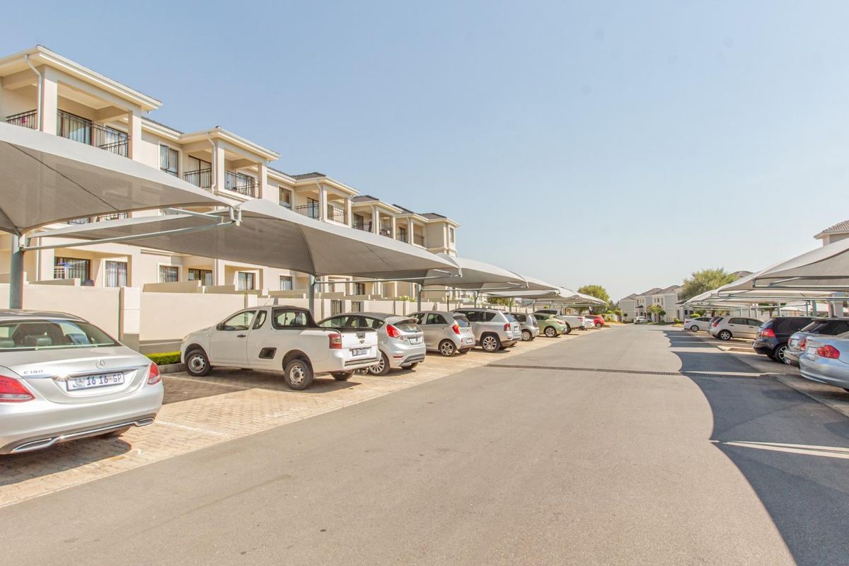 Exterior view of the apartment complex parking area featuring paved bays and shade cloth carports.