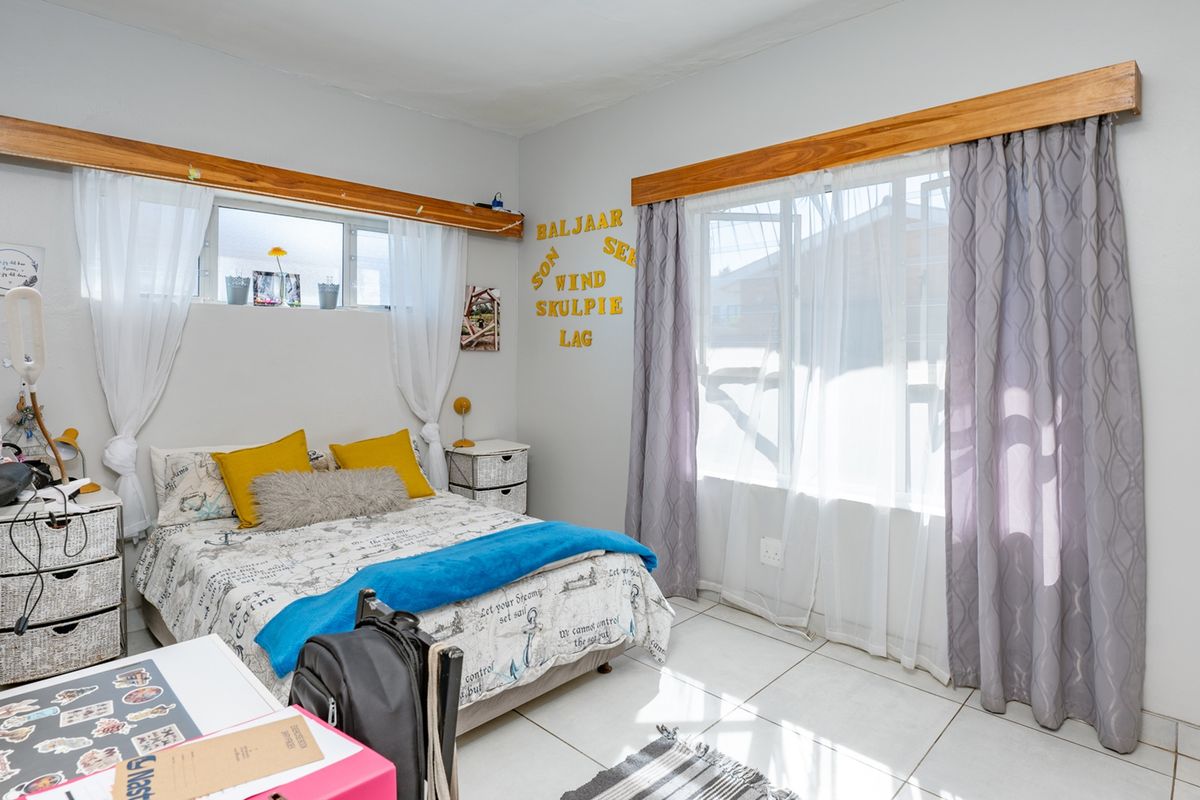 A bright bedroom featuring tiled flooring, built-in wooden curtain pelmets, and integrated wardrobe storage, offering a functional and well-lit living space.