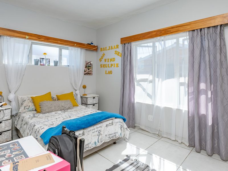 A bright bedroom featuring tiled flooring, built-in wooden curtain pelmets, and integrated wardrobe storage, offering a functional and well-lit living space.