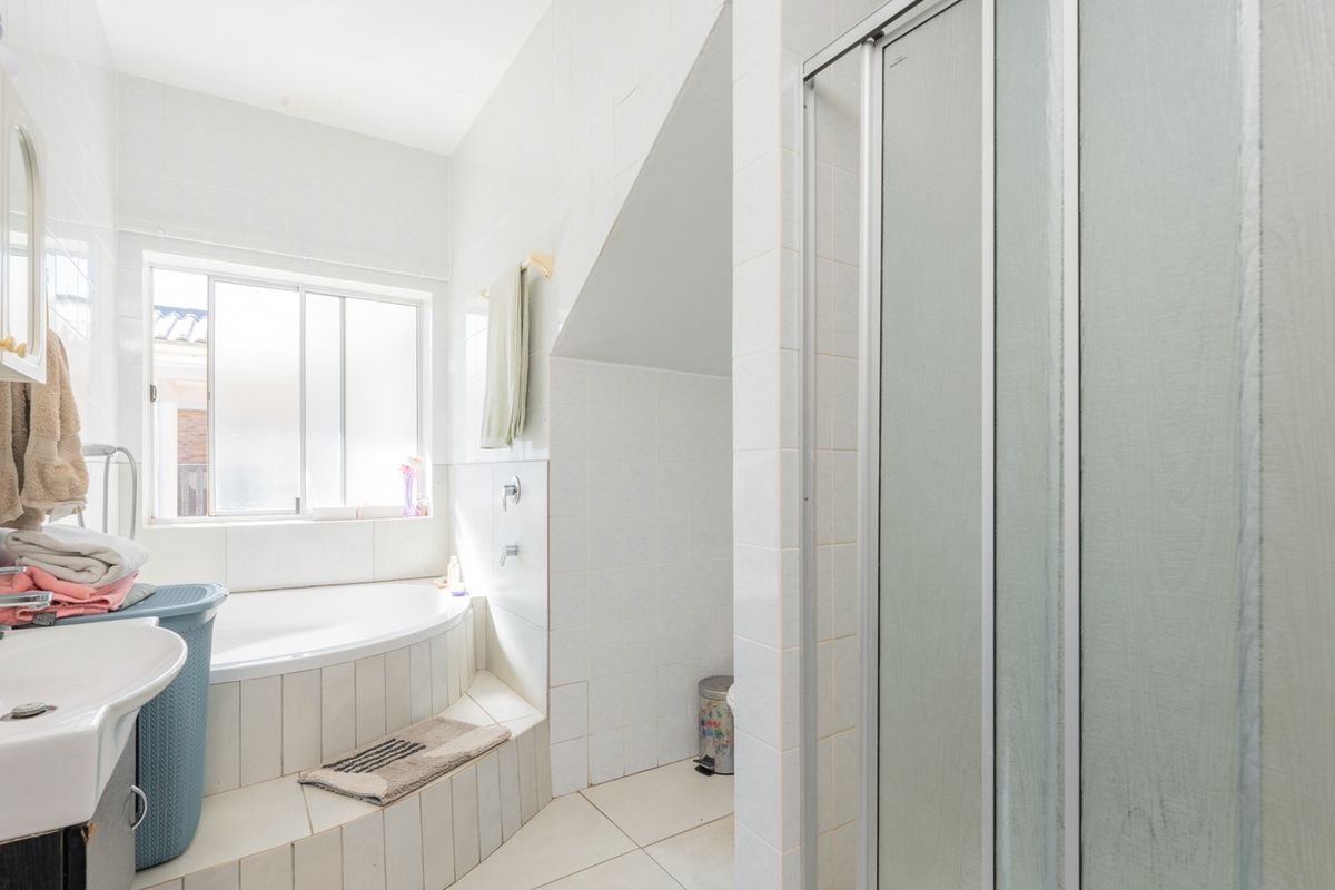 A functional bathroom featuring a built-in bathtub, separate shower enclosure, and pedestal basin with tiled finishes throughout.