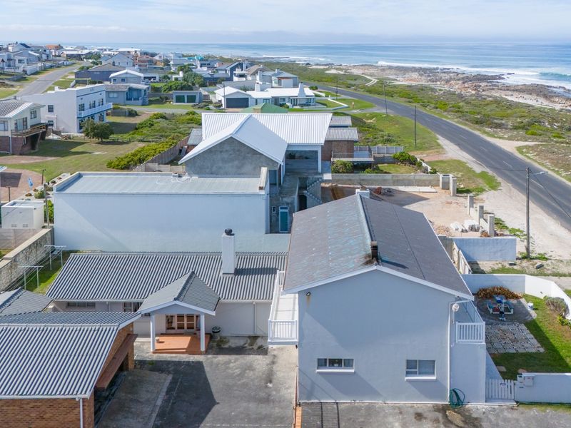 Aerial view of a coastal residential property featuring multiple roof structures, a paved driveway, and proximity to the ocean.