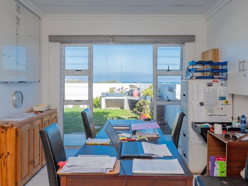 A functional home office space featuring tiled flooring, built-in cabinetry, and large windows providing natural light and views of the garden.