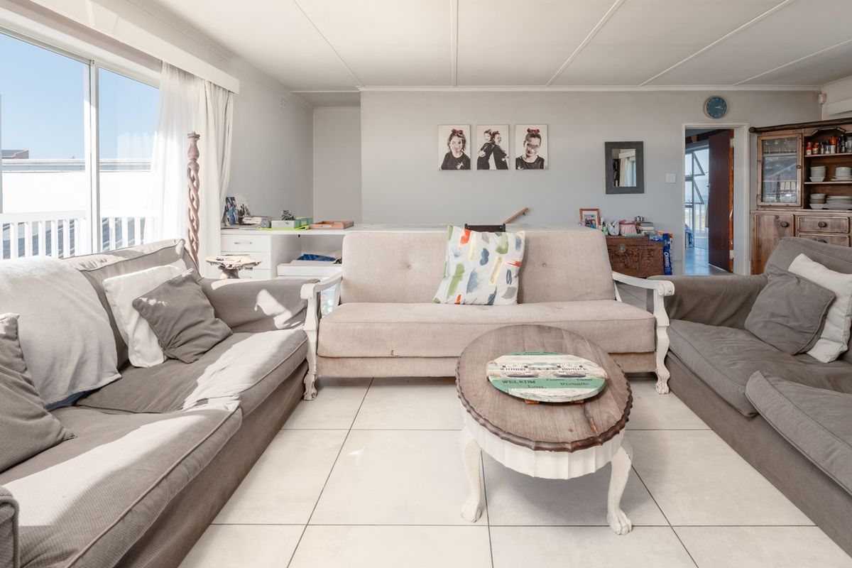 A bright living room featuring large sliding glass doors, neutral tiled flooring, and a functional layout with access to adjacent areas.