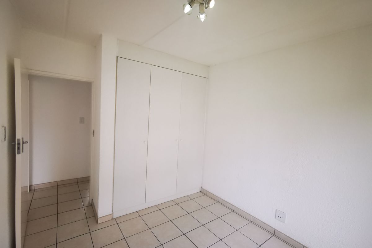 A vacant bedroom featuring neutral tiled flooring, built-in cupboards, and a central ceiling light fixture, offering a clean and simple living space.