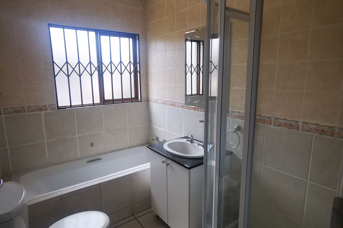 A functional bathroom featuring a built-in bathtub, a separate glass-enclosed shower, a vanity basin, and a toilet with security bars on the window.