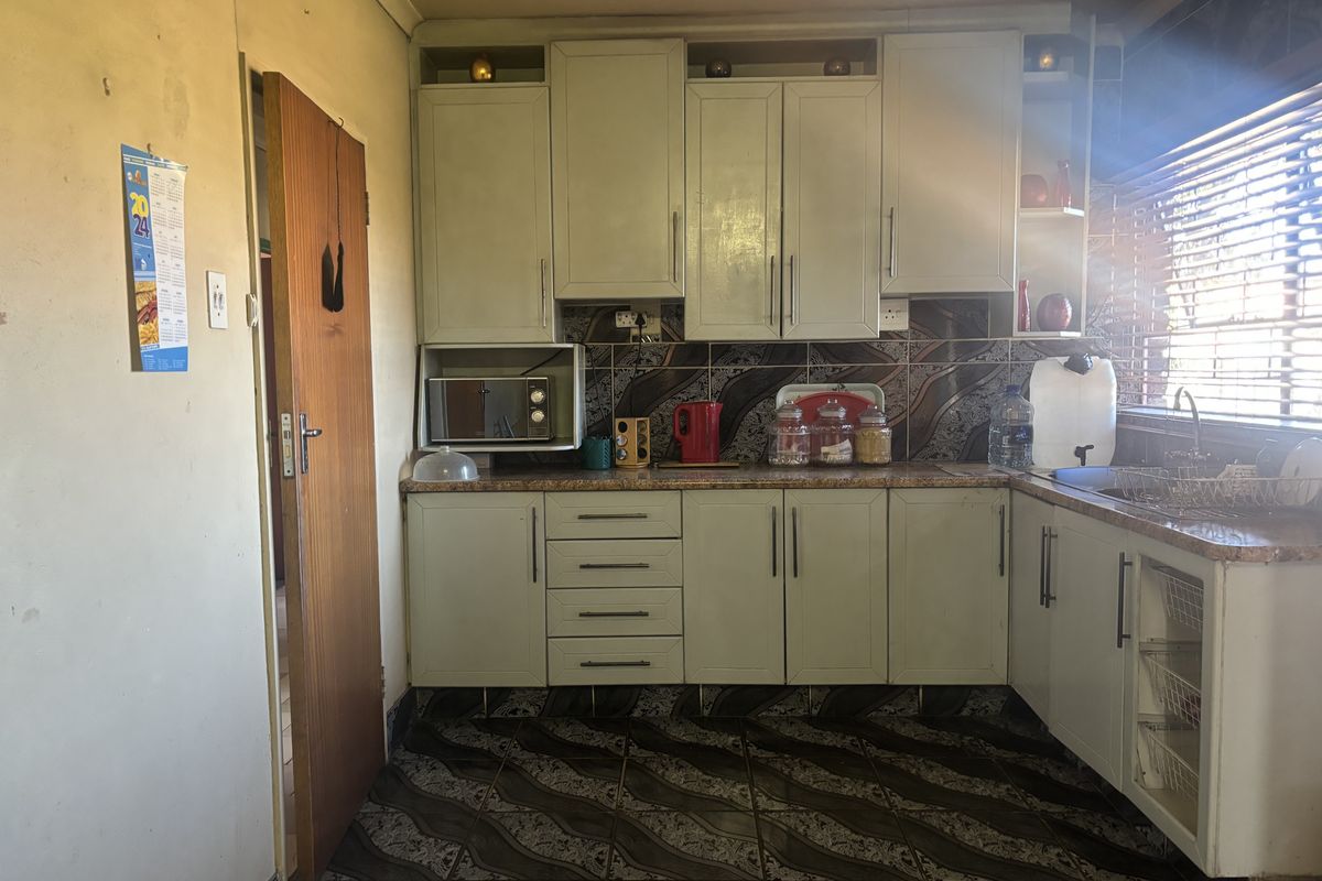 A dated kitchen featuring built-in cabinetry, tiled backsplash, and tiled flooring, requiring cosmetic updates to modernize the space.