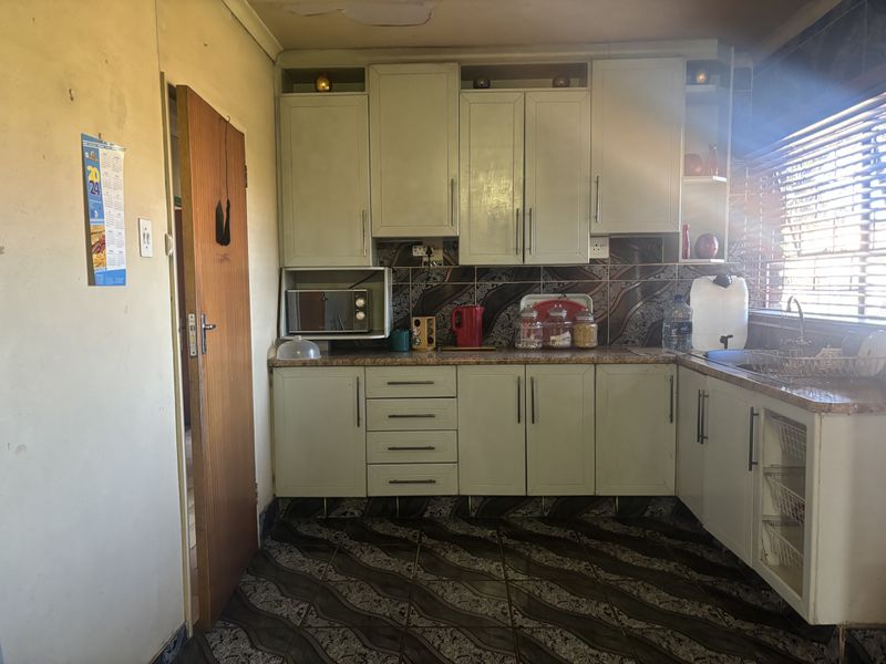 A dated kitchen featuring built-in cabinetry, tiled backsplash, and tiled flooring, requiring cosmetic updates to modernize the space.