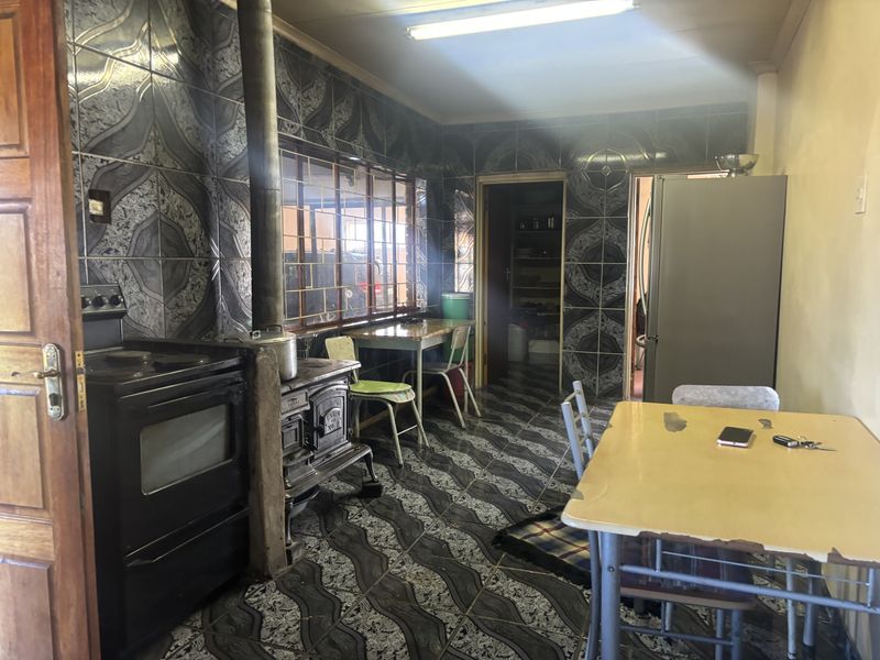 Kitchen featuring dated patterned wall and floor tiles, a built-in stove, and a traditional cast iron wood-burning stove with a flue.