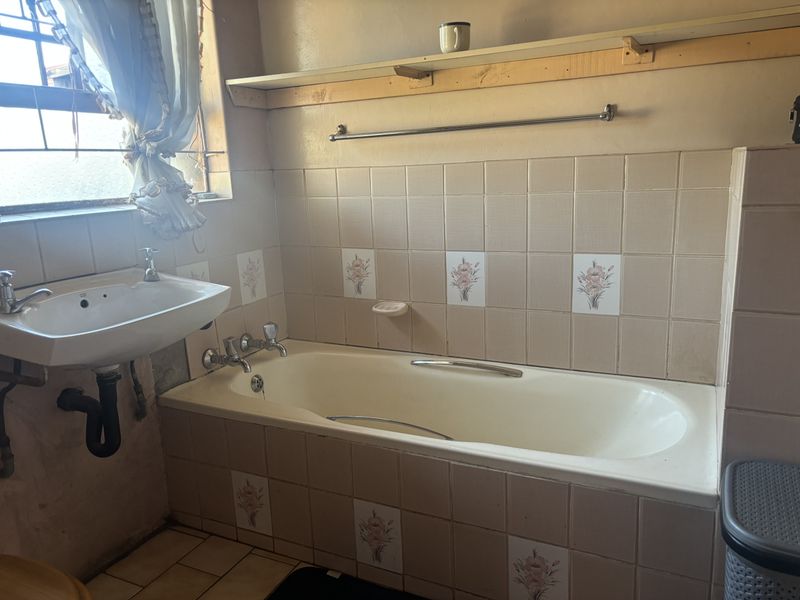 A dated bathroom featuring a built-in bathtub, wall-mounted basin, and decorative tiled splashbacks, offering potential for a modern renovation.