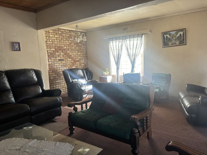 Spacious living room featuring an exposed brick accent wall, timber ceiling details, and carpeted flooring, offering a traditional layout with natural light.