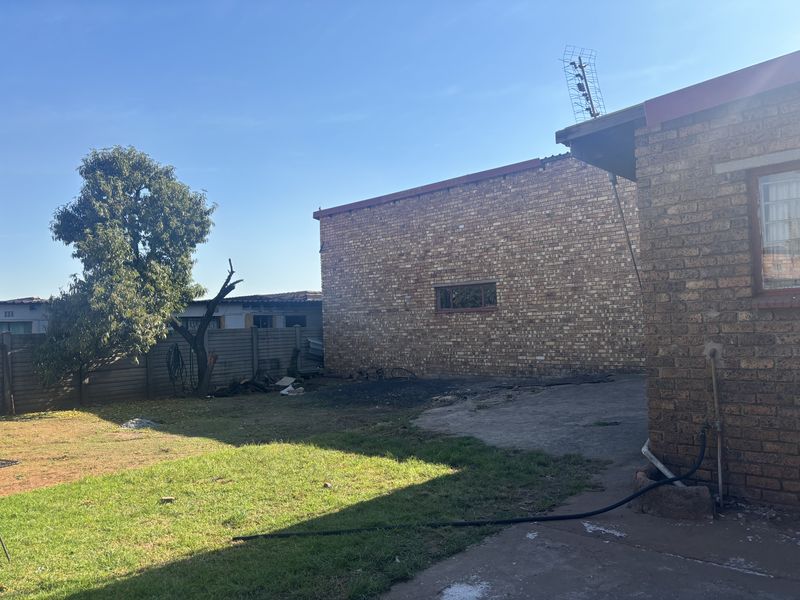 Rear exterior view of the property featuring face brick walls, a concrete apron, and a spacious backyard area with boundary walling.