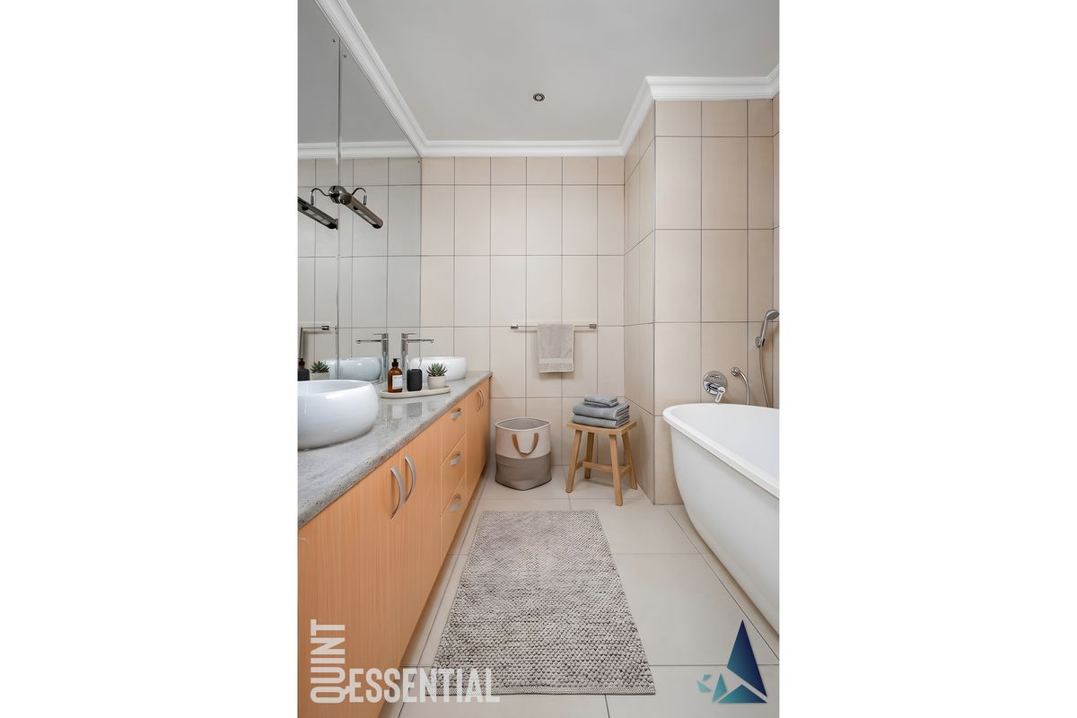 Modern bathroom featuring a sleek vanity with dual vessel sinks, a large mirror, and a freestanding bathtub with neutral wall tiling.