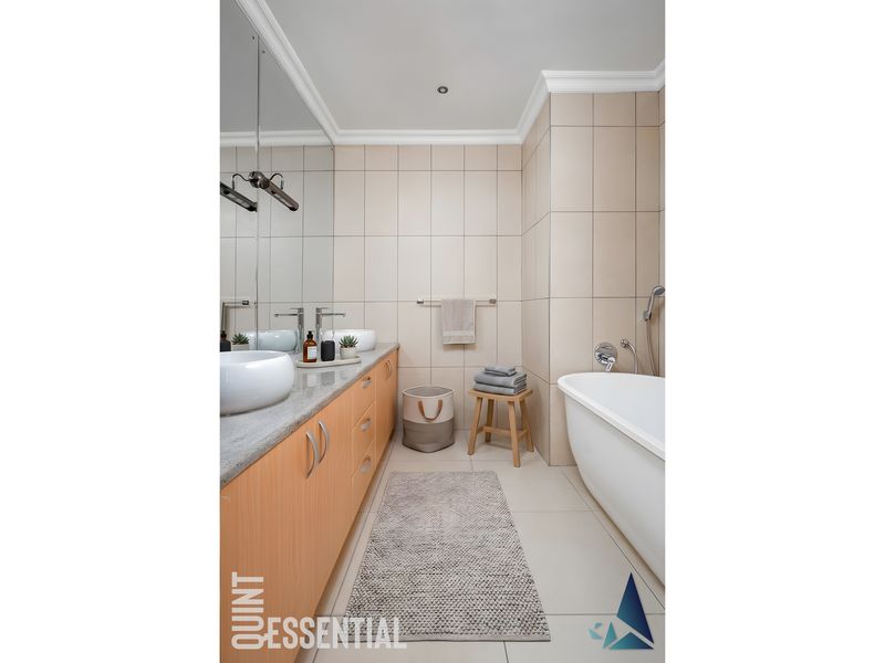 Modern bathroom featuring a sleek vanity with dual vessel sinks, a large mirror, and a freestanding bathtub with neutral wall tiling.