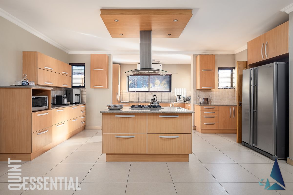 Spacious kitchen featuring light wood cabinetry, a central island with a gas hob, granite countertops, and tiled flooring throughout.