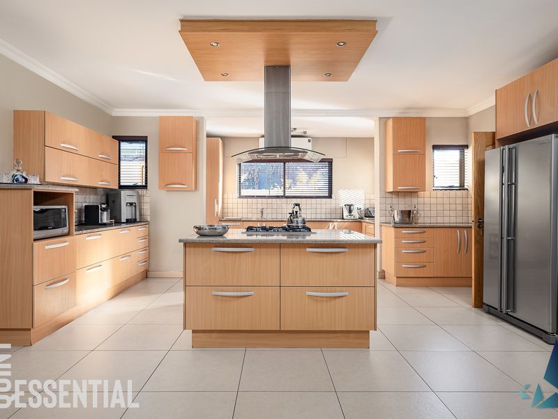 Spacious kitchen featuring light wood cabinetry, a central island with a gas hob, granite countertops, and tiled flooring throughout.