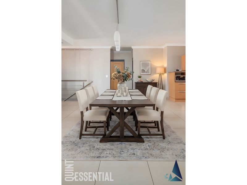 A well-lit dining area featuring tiled flooring, adjacent to a modern kitchen with built-in cabinetry and oven, and a staircase with a metal railing.