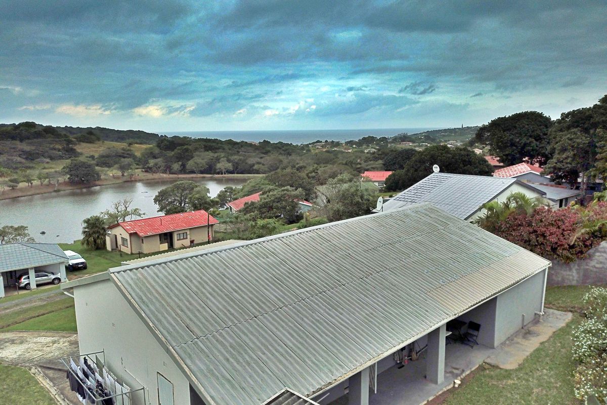 Aerial view of a residential property featuring a corrugated metal roof and a covered patio area, overlooking a scenic landscape with a lake.