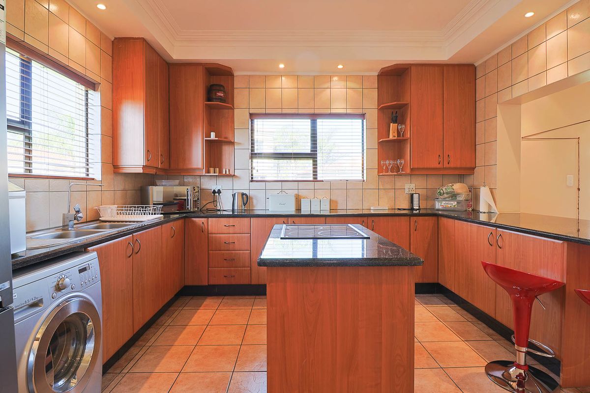 A functional kitchen featuring wooden cabinetry, granite countertops, a central island with a built-in hob, and tiled flooring.