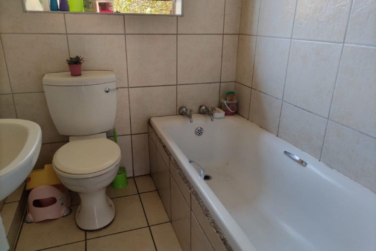 A functional bathroom featuring a standard bathtub, toilet, and pedestal basin with neutral ceramic wall and floor tiling.