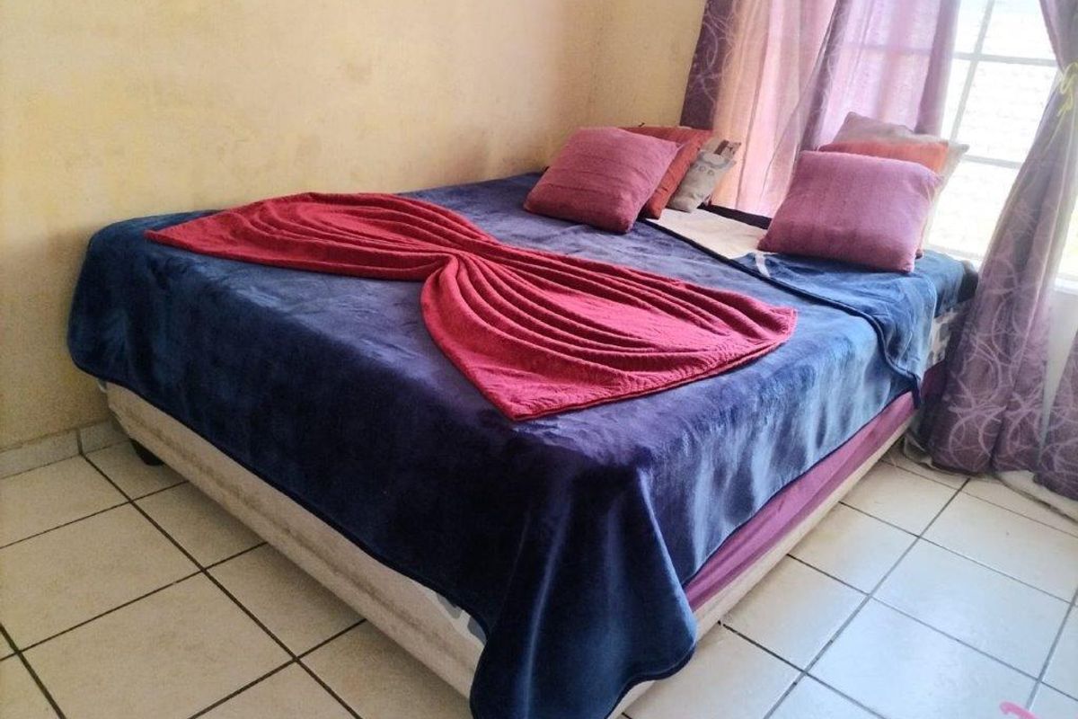 A bedroom featuring tiled flooring and a window, currently showing signs of wear on the wall surfaces.