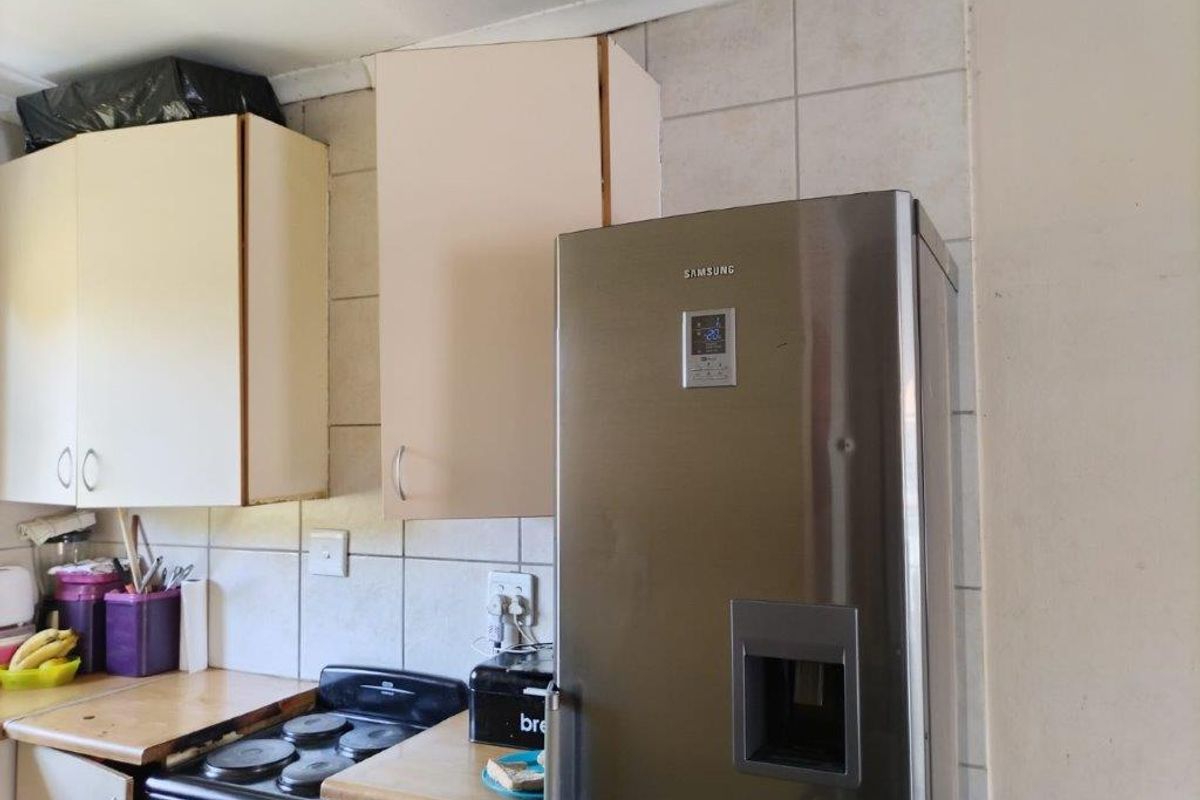 A functional kitchen area featuring built-in cabinetry, a tiled backsplash, and laminate countertops, currently showing signs of wear and dated finishes.