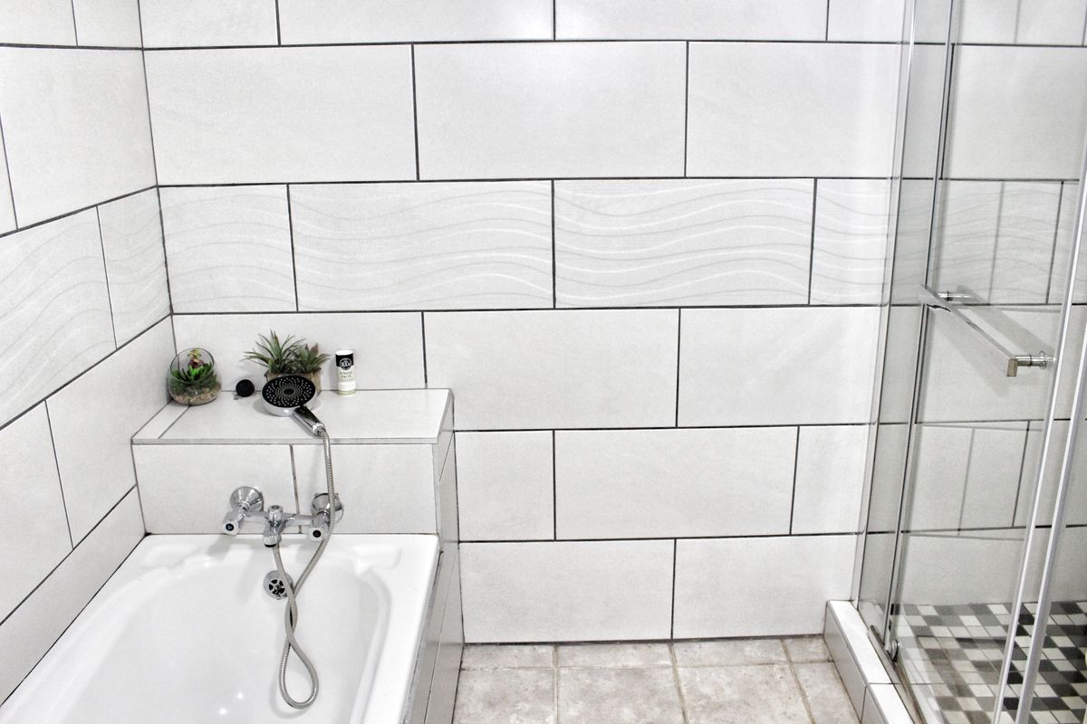 A modern bathroom featuring a built-in bathtub with chrome mixer and a separate glass-enclosed shower with neutral wall and floor tiling.