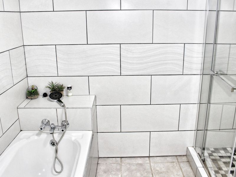 A modern bathroom featuring a built-in bathtub with chrome mixer and a separate glass-enclosed shower with neutral wall and floor tiling.