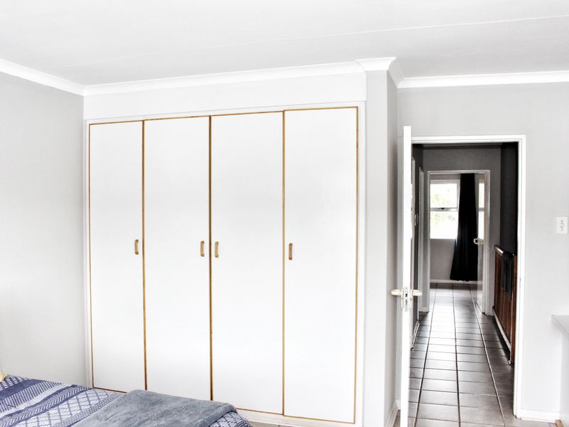A bedroom featuring built-in cupboards with white doors and gold trim, leading into a tiled hallway.